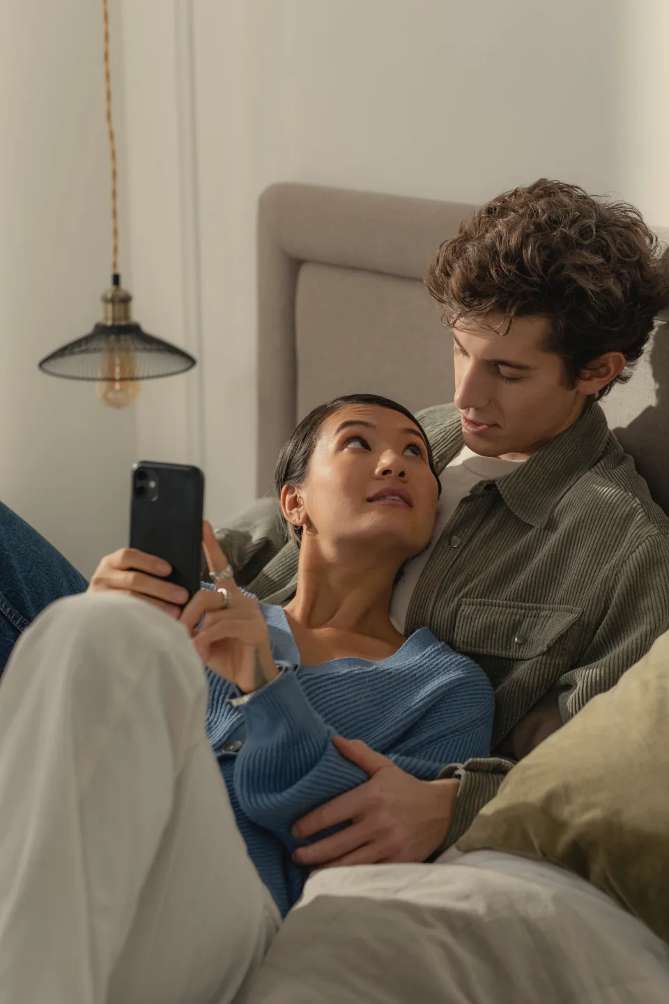 Couple regardant ensemble des souvenirs sur un smartphone, allongés dans leur lit.