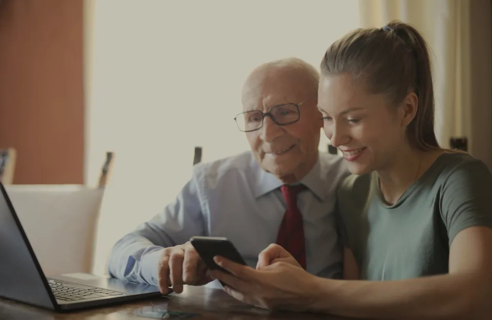 Homme âgé et jeune femme souriants, regardant ensemble un smartphone.